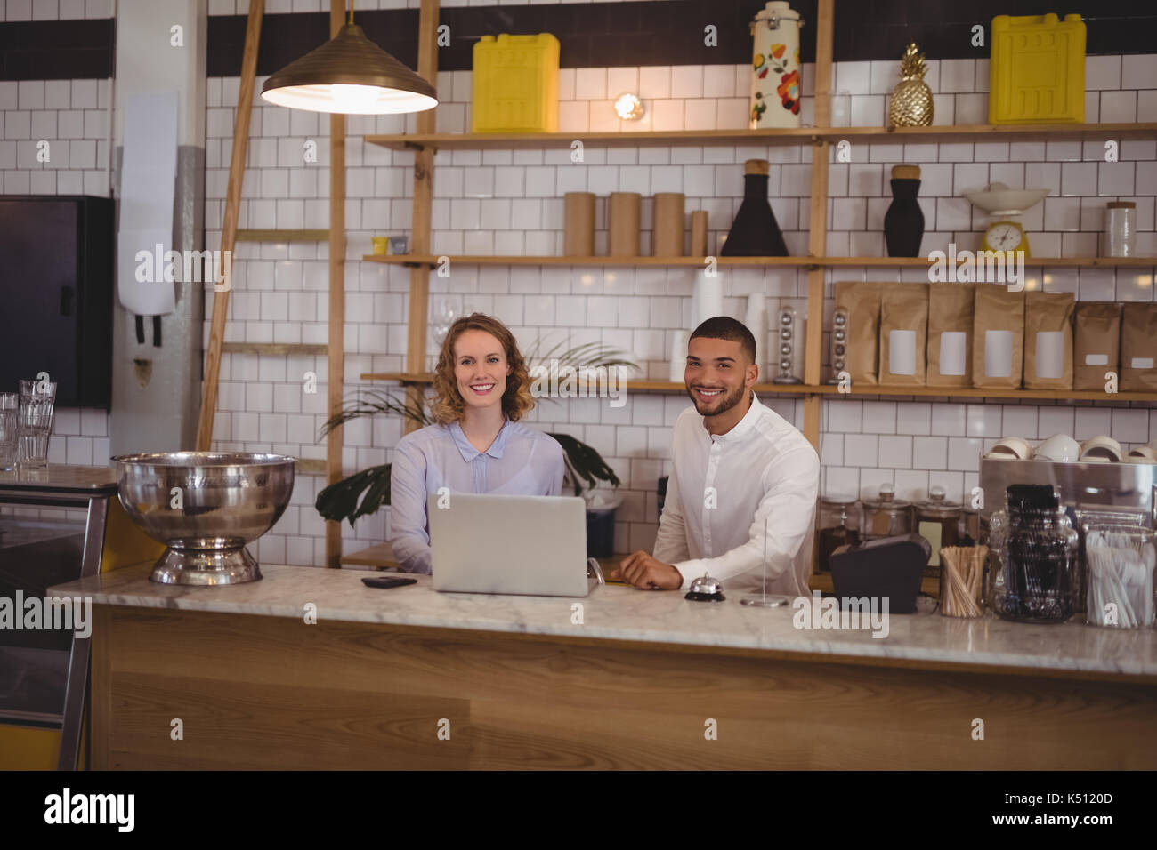 Portrait von lächelnden Kellnerin und männlichen Eigentümer mit Laptop an der Theke im Café Stockfoto