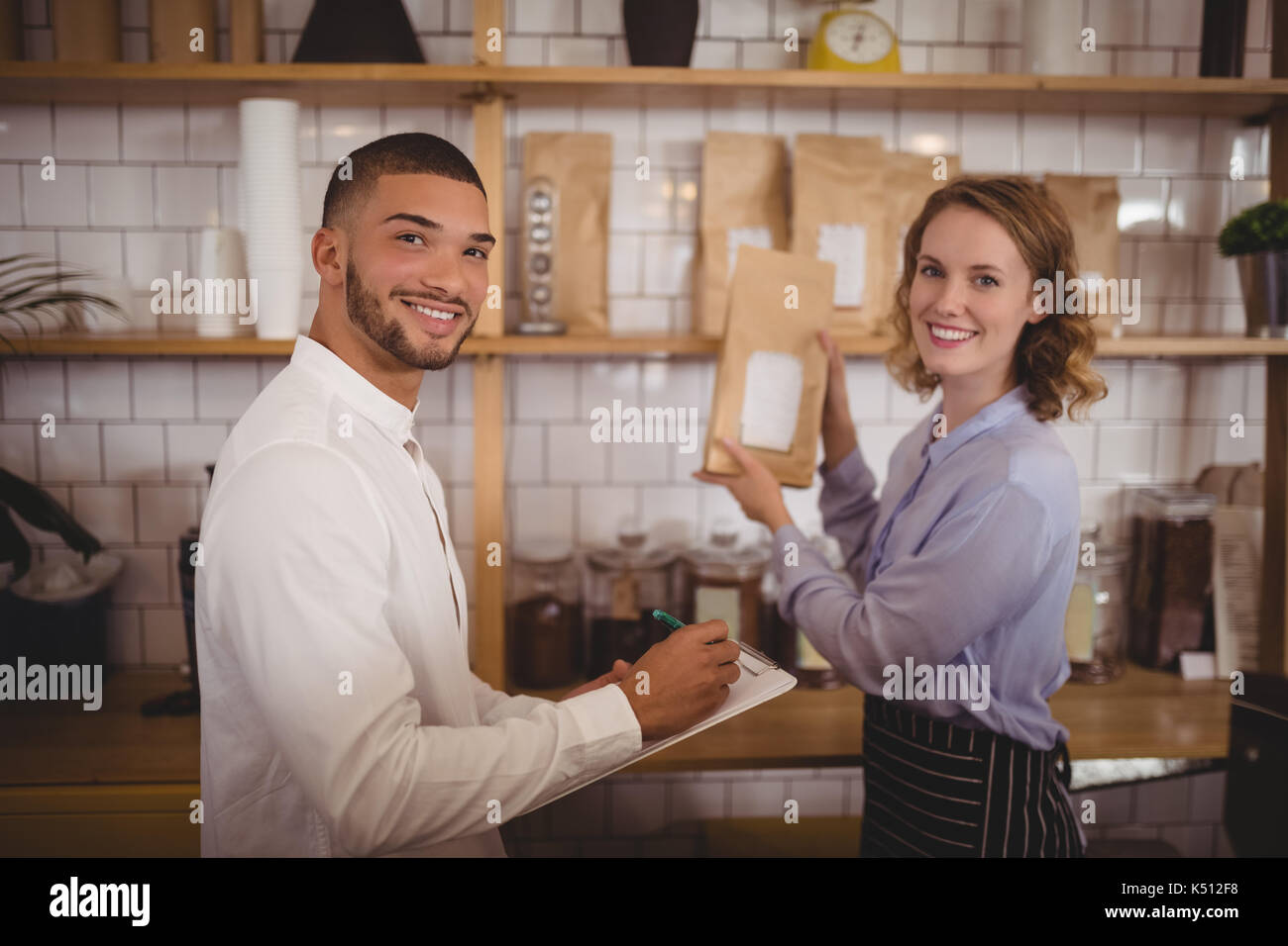 Portrait von lächelnden Mann Eigentümer und Kellnerin, die die Pakete auf dem Regal im Coffee Shop Stockfoto