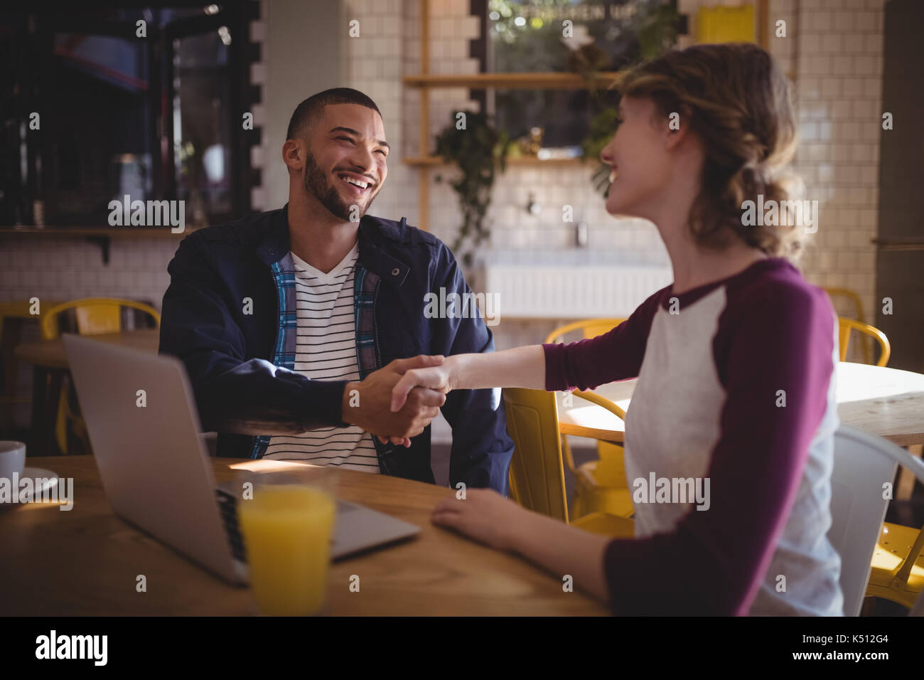 Lächelnden jungen Freunde die Hände schütteln beim Sitzen mit Laptop im Coffee Shop Stockfoto