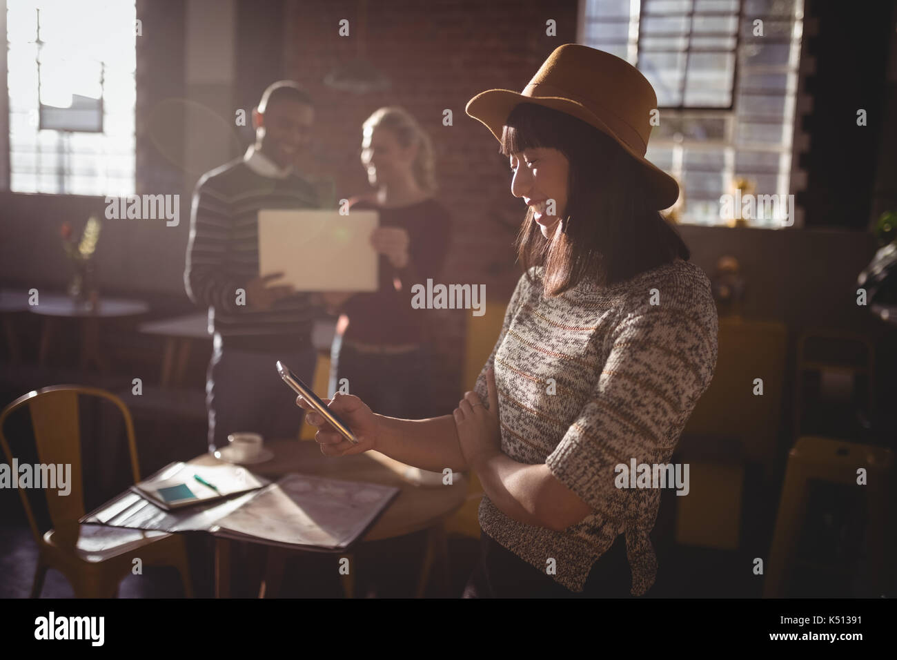 Lächelnde Frau mit Smartphone gegen colleauges im Coffee shop Stand Stockfoto