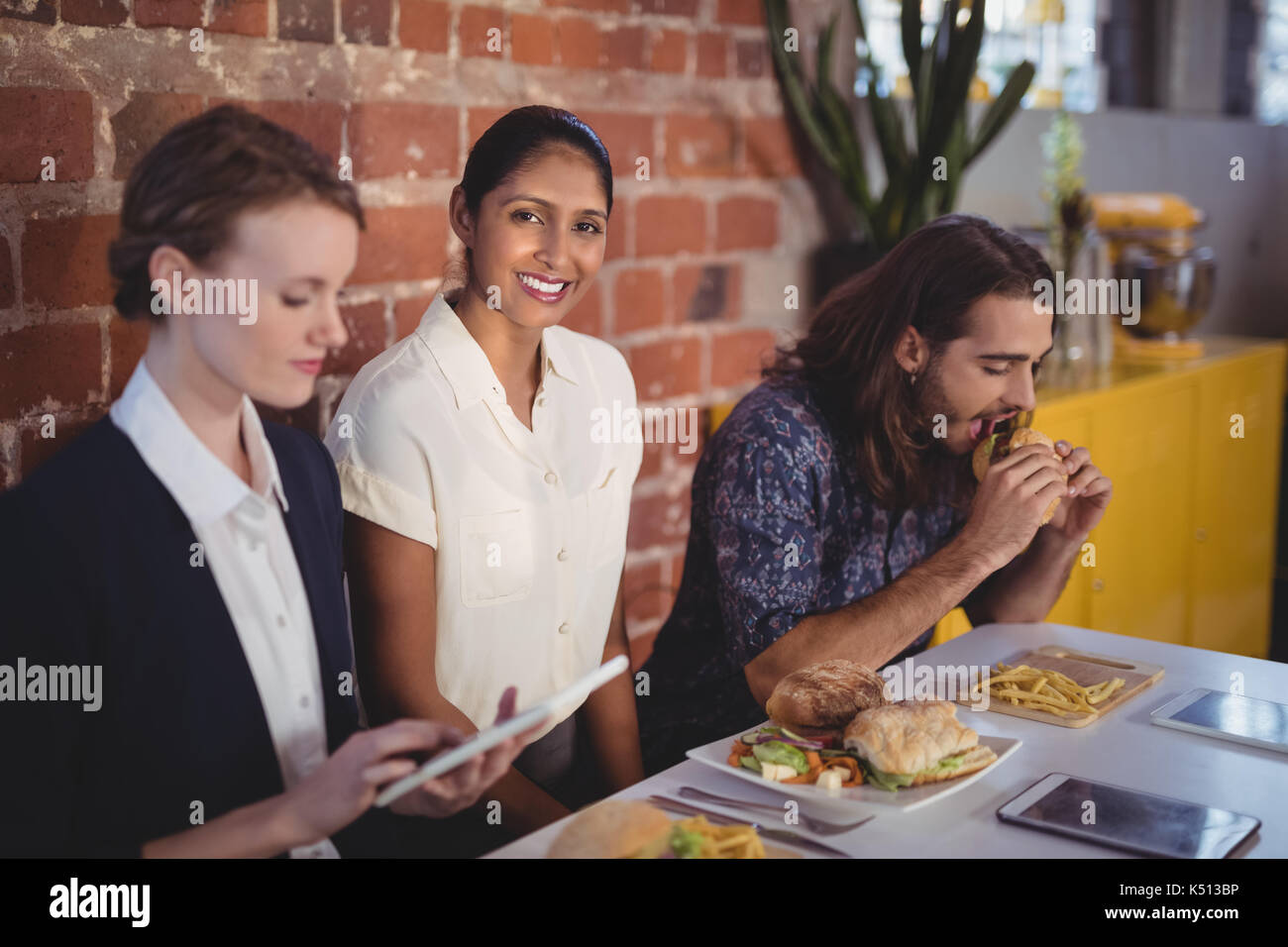 Portrait von lächelnden jungen Frau sitzt inmitten von Freunden am Tisch mit Essen im Coffee Shop Stockfoto
