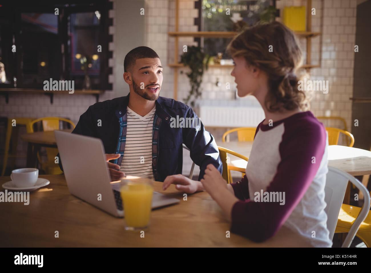 Junge Freunde sprechen beim Sitzen mit Laptop und Getränke im Coffee Shop Stockfoto