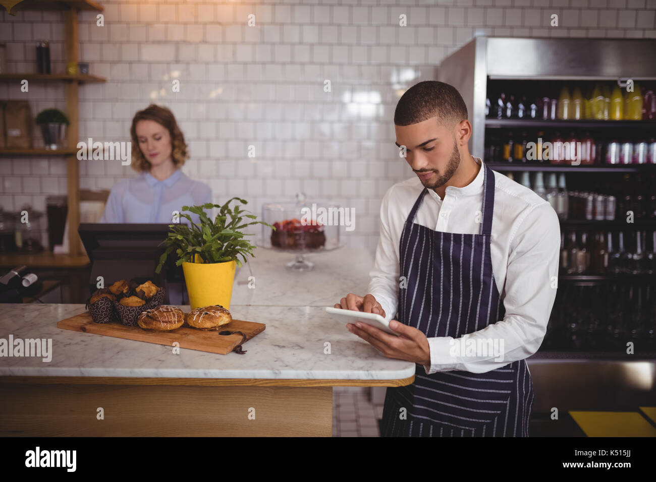 Junger Kellner mit digitalen Tablet im Stehen durch Zähler in Coffee Shop Stockfoto