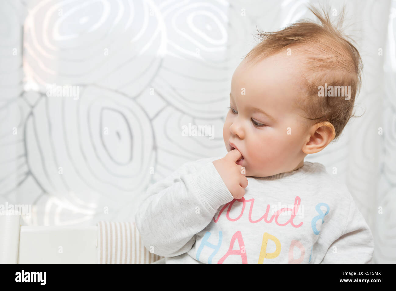 Elf Monate alten Baby Mädchen in einem Hocker, lustige Gesichter in die Kamera sitzt, überrascht und ihr Finger klemmt im Mund Stockfoto