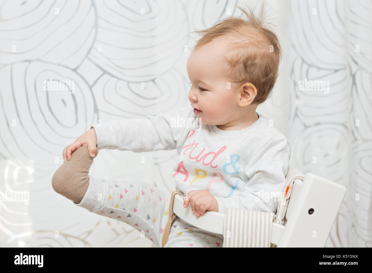 Elf Monate alten Baby Mädchen in einem Stuhl sitzend, ziehen ihre Socke aus ihren Füßen Stockfoto