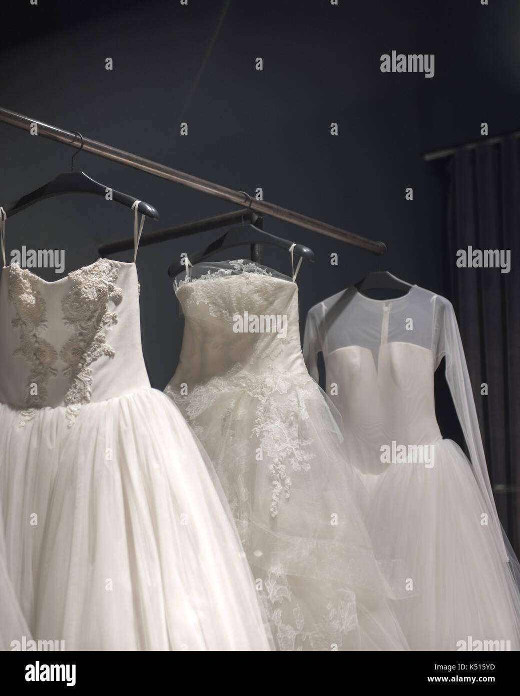 Auswahl an handgefertigten weisse Hochzeit Kleider hängen auf einer Schiene in einem abgedunkelten Raum teilweise von einem Licht beleuchtet Stockfoto