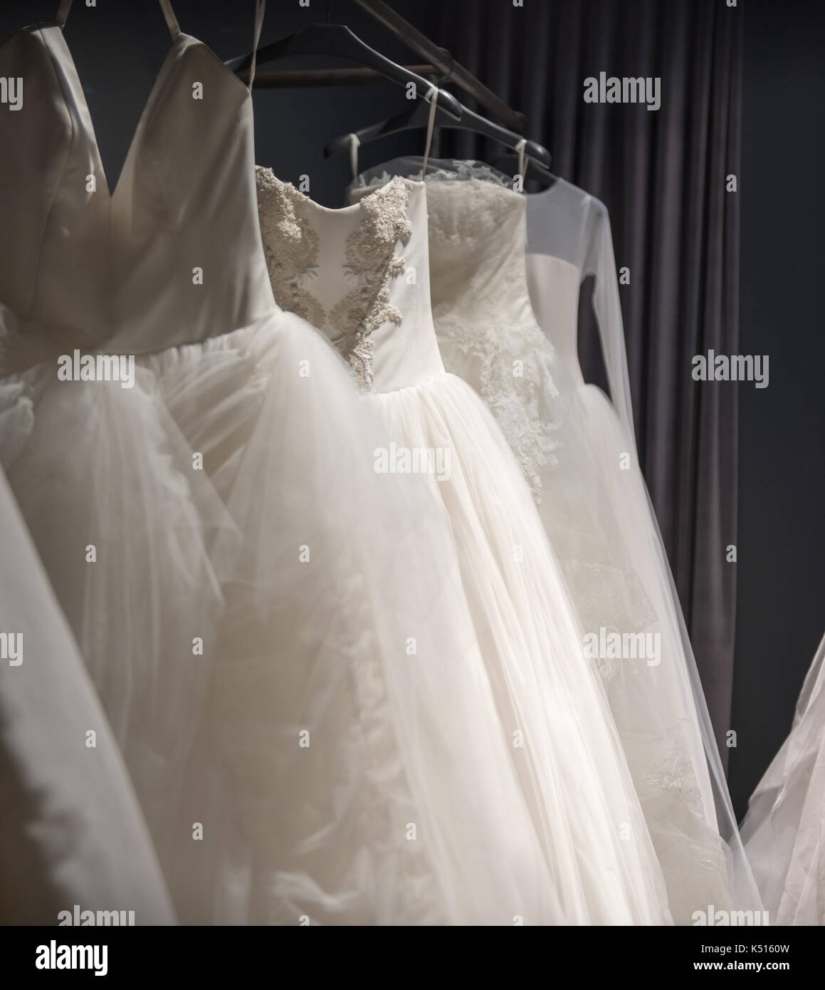 Auswahl an handgefertigten weisse Hochzeit Kleider hängen auf einer Schiene in einem abgedunkelten Raum teilweise von einem Licht beleuchtet Stockfoto
