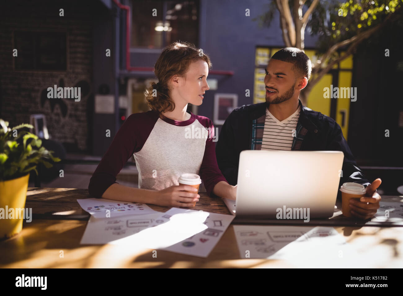 Junge kreative Fachleute sprechen beim Sitzen mit Laptop am Tisch im Café Stockfoto