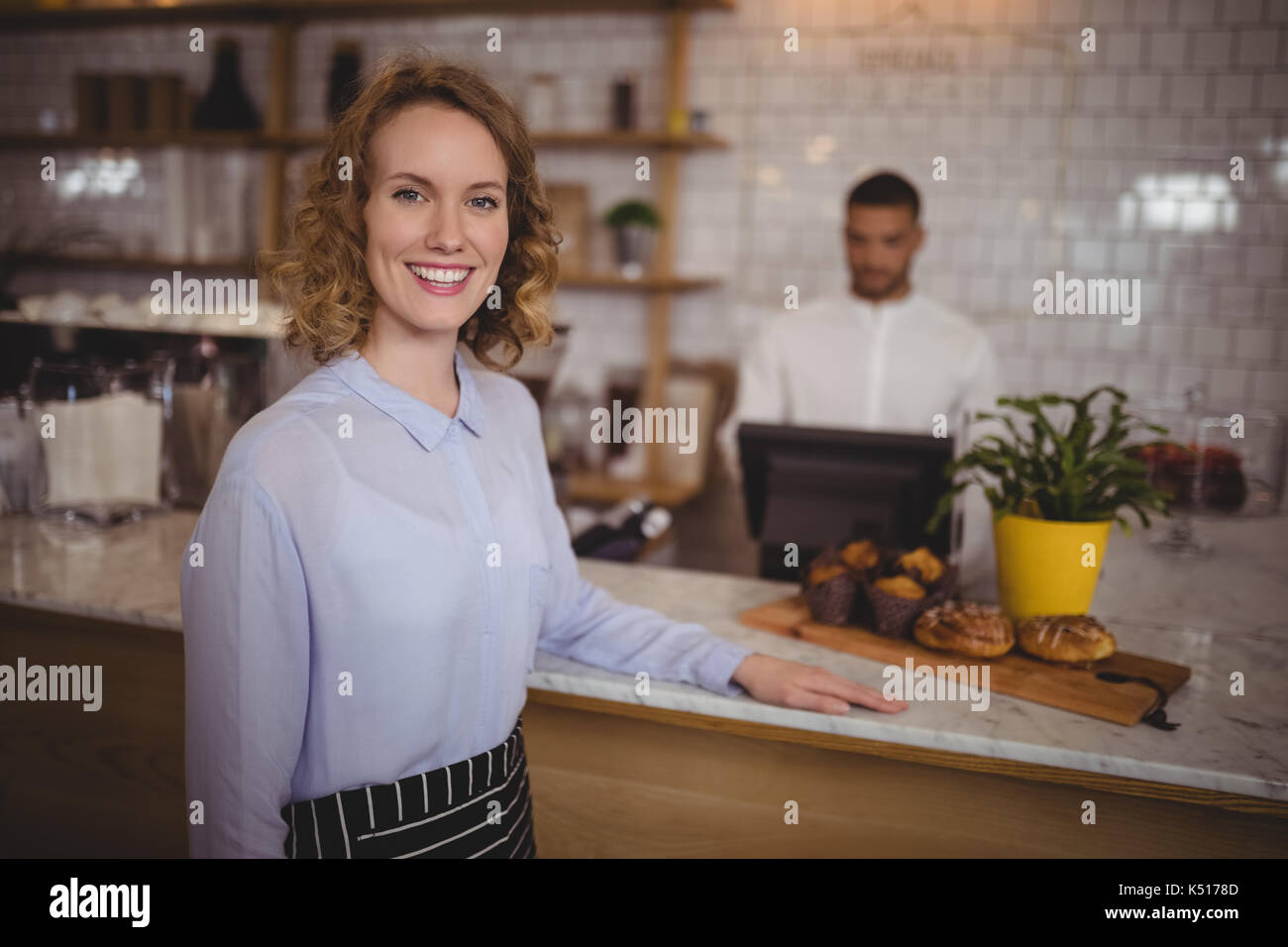 Portrait von zuversichtlich Kellnerin stehend durch Zähler bei Coffee Shop Stockfoto