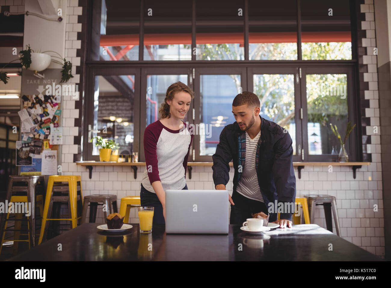 Mann deutete auf Laptop im Stehen durch Frau in Coffee Shop Stockfoto