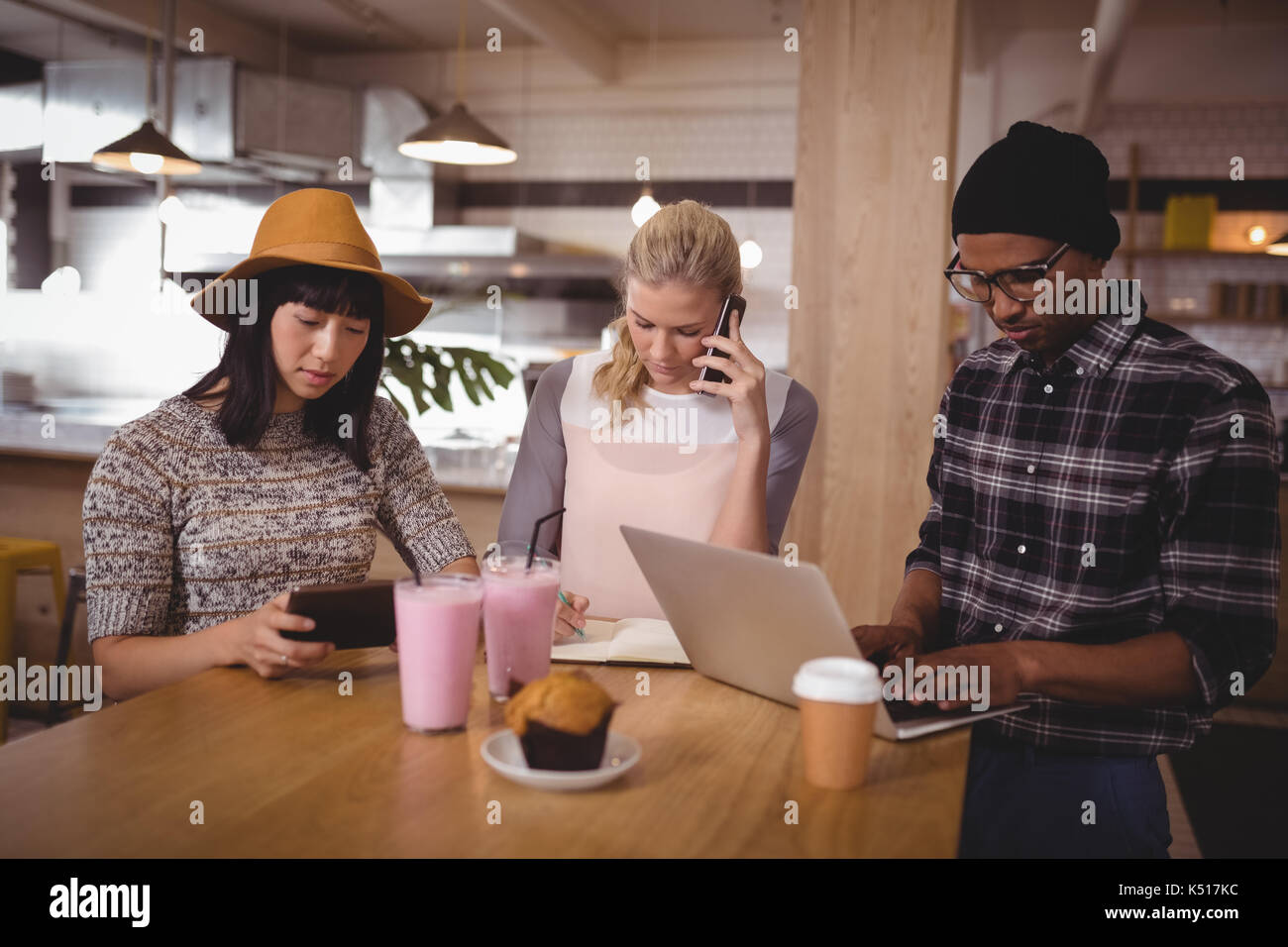 Junge Freunde sitzen am Tisch während der Verwendung von Technologien in Coffee Shop Stockfoto