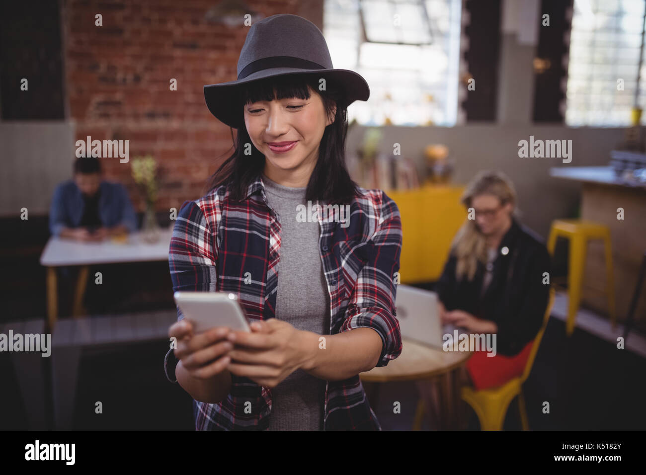 Lächelnde junge attraktive Frau mit Handy während Coffee Shop Stand Stockfoto