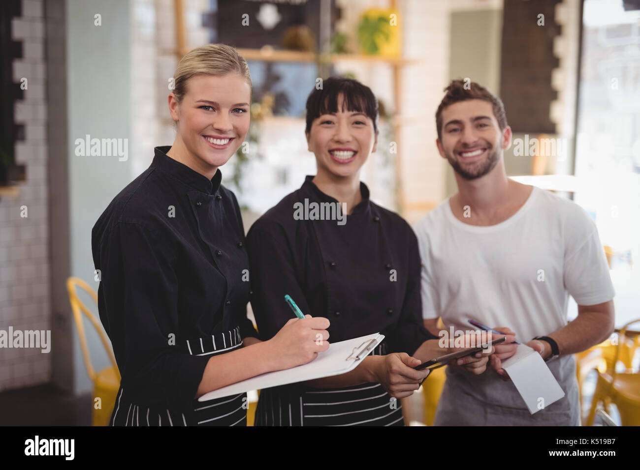 Portrait von fröhlicher junger Mitarbeiter warten Holding digital Tablet mit Notepad und Zwischenablage an Coffee Shop Stockfoto