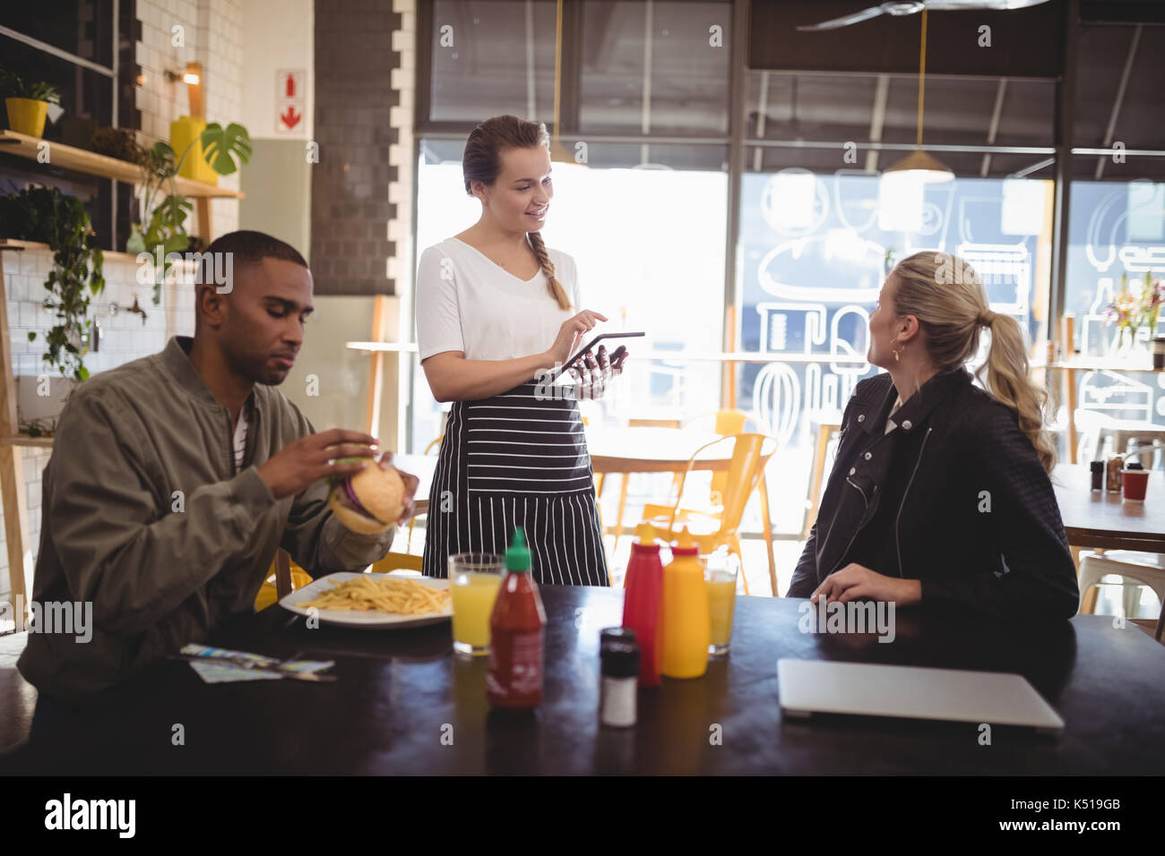 Junge Frau zu Essen bestellen Kellnerin beim Sitzen mit männlichen Freund im Cafe Stockfoto