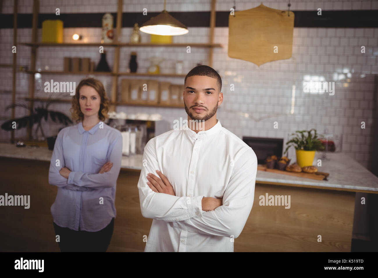 Portrait von selbstbewussten jungen Mann mit verschränkten Armen stehend gegen Frau an Coffee Shop Stockfoto