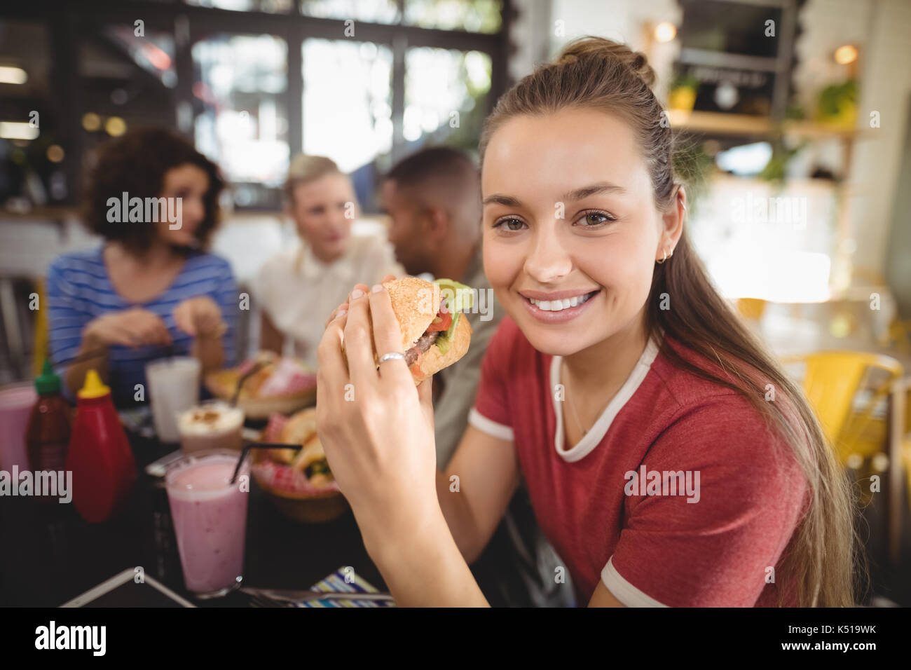 Close up Portrait von lächelnden schönen jungen Frau burger Essen im Coffee Shop Stockfoto