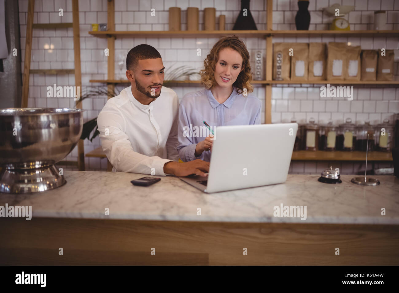 Männliche Inhaber und junge Kellnerin mit Laptop sitzen an der Theke im Café Stockfoto