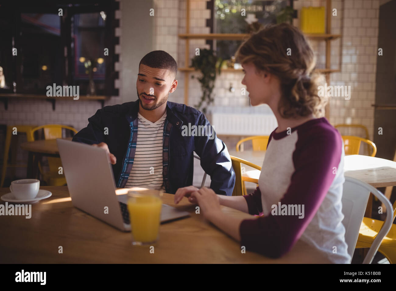 Junger Mann deutete auf Laptop während der Sitzung durch Frau in Coffee Shop Stockfoto