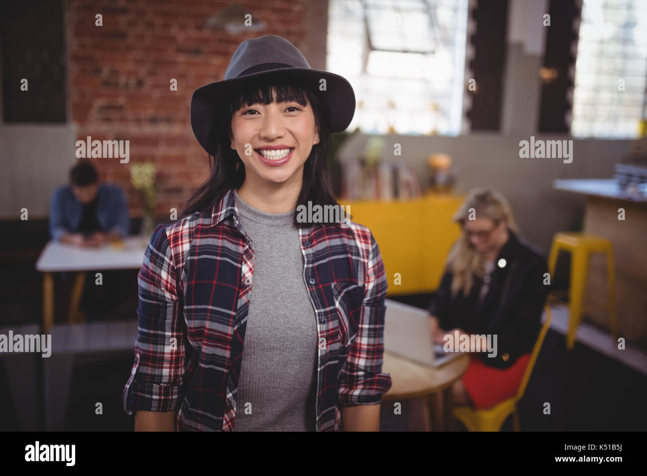 Portrait von lächelnden jungen Frau mit Hut stehend an Coffee Shop Stockfoto