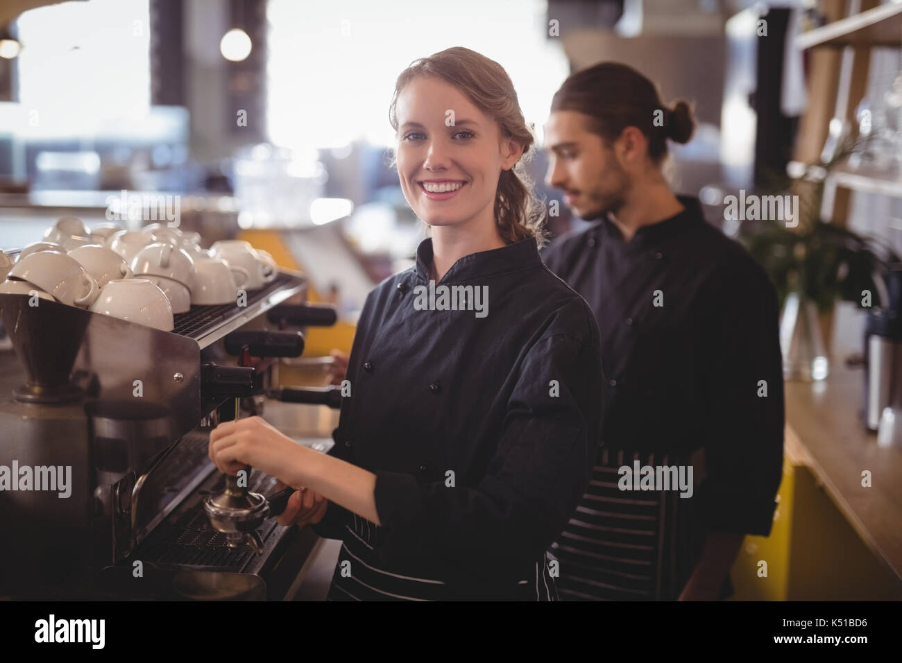Portrait von lächelnd weibliche Barista mit Espressomaschine gegen Kellner im Café Stockfoto