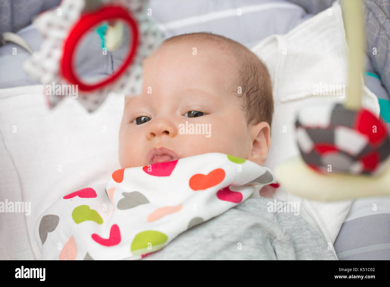 Neugeborenes Mädchen in einem rockigen Sitz mit Spielzeug über Ihrem Kopf hängenden Niedlich, ihre Aufmerksamkeit Grabbing Stockfoto
