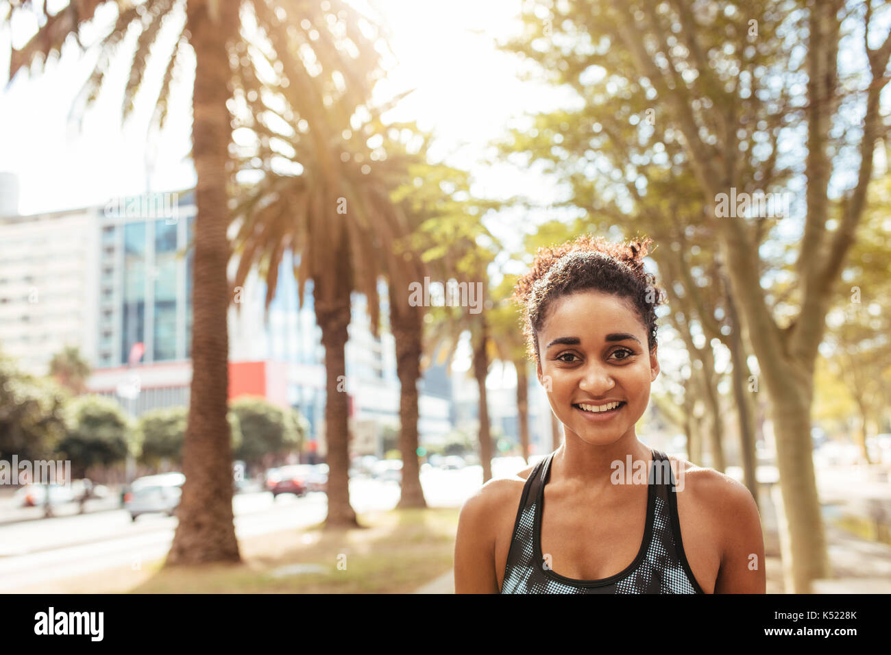 Lächelnde junge Frau im lockigen Haar für ein Foto posieren. Frau im laufenden Outfit im Freien. Stockfoto