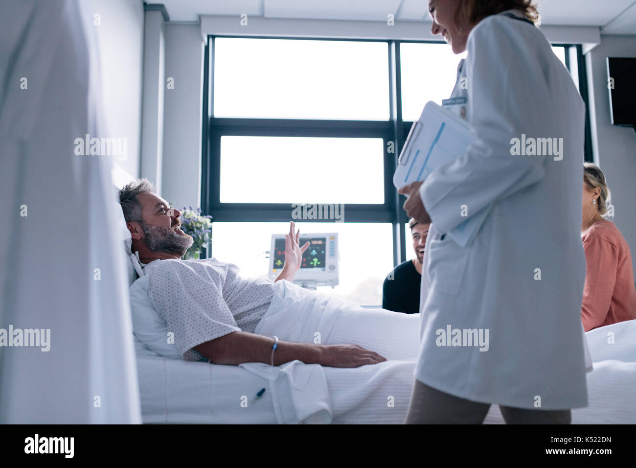 Frau Doktor, Patient im Krankenhaus. Kranken Mann im Bett lag, mit der Familie zu sitzen, und Arzt. Stockfoto