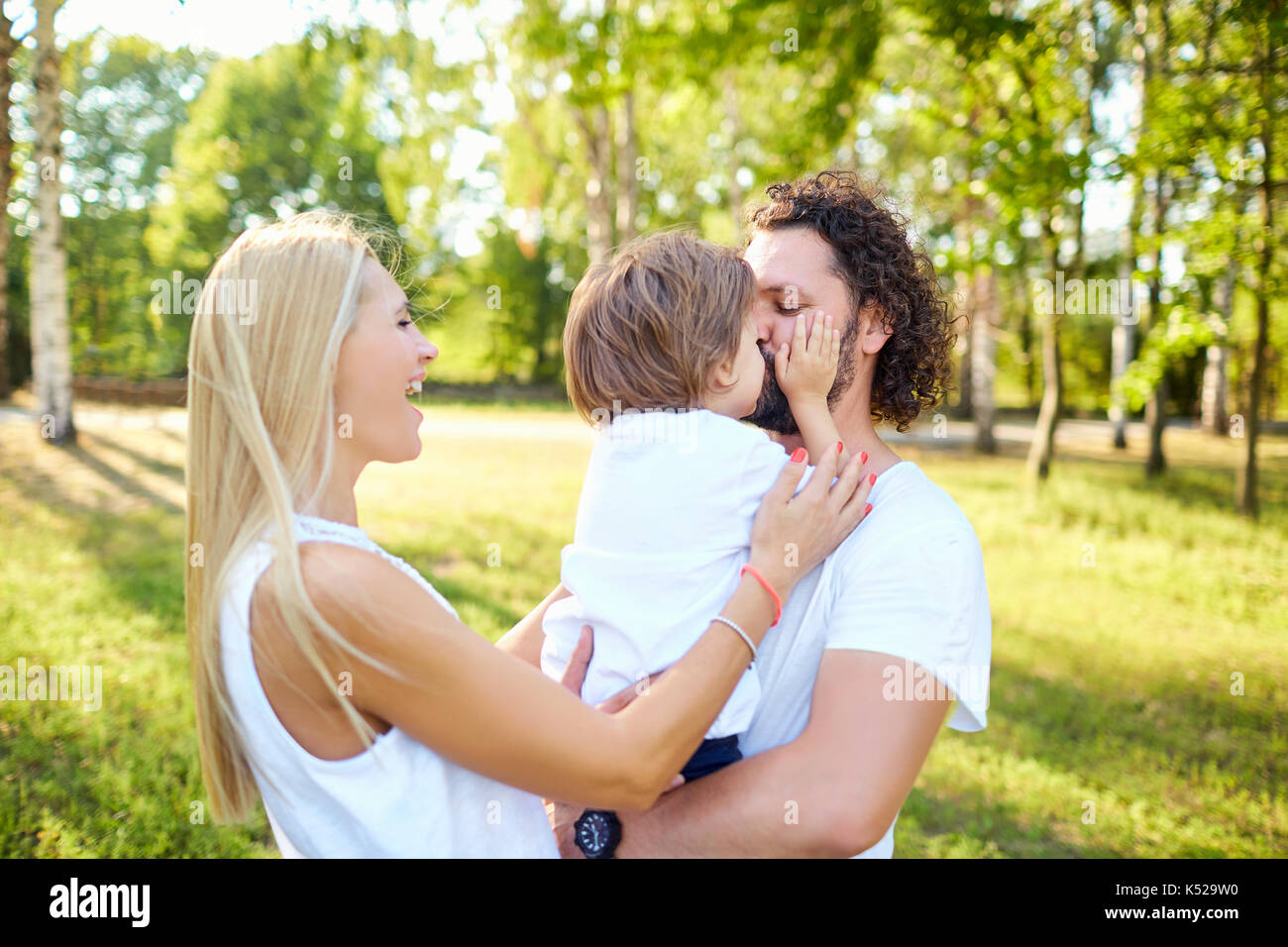 Vater und Mutter, umarmen, küssen ein Kind im Park in der Summe Stockfoto Vater und Mutter, umarmen, küssen ein Kind im Park in der Summe Stockfoto