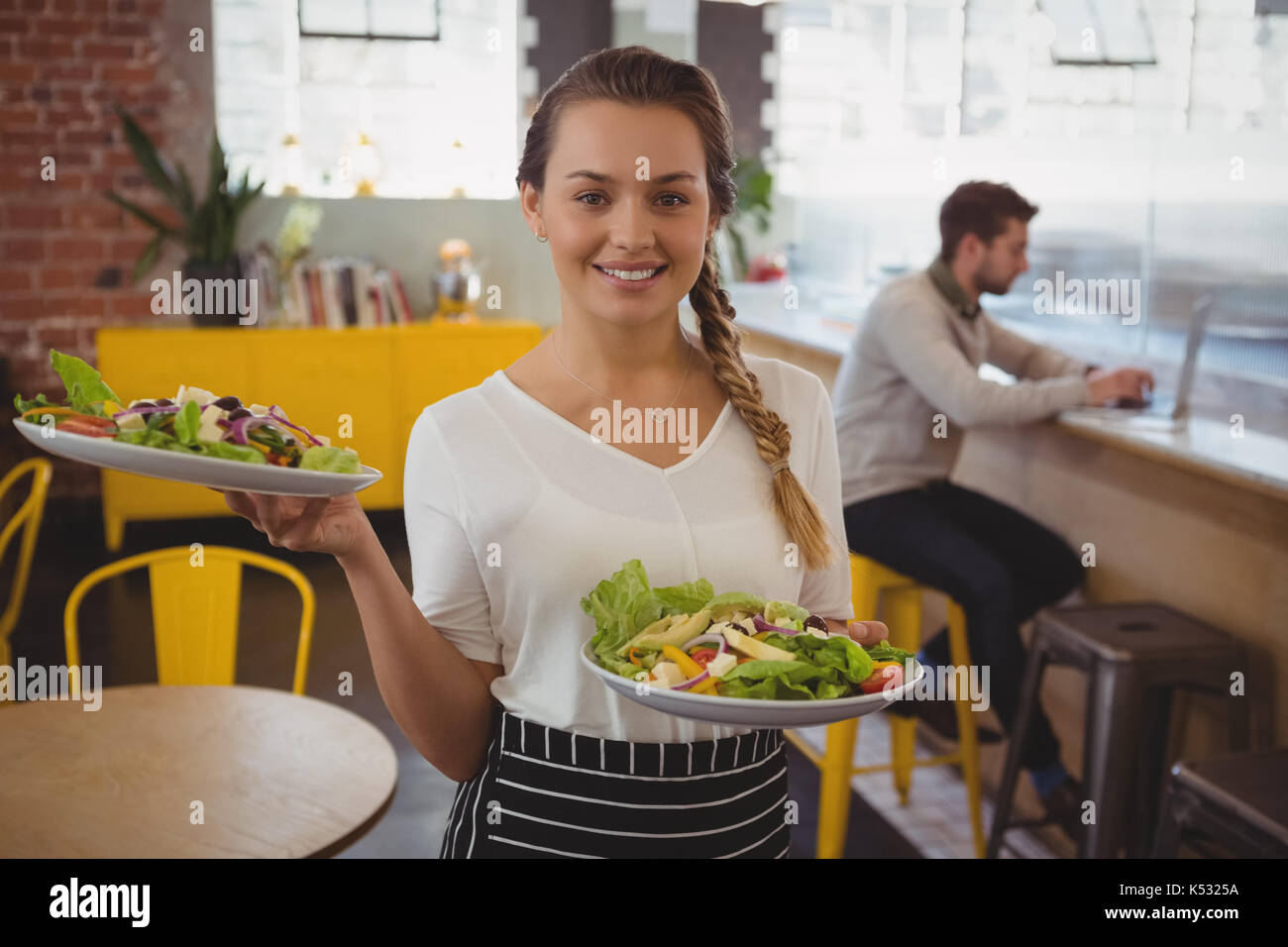 Portrait von Kellnerin Haltebleche mit Salat, während Unternehmer mit Laptop an der Theke im Cafe Stockfoto