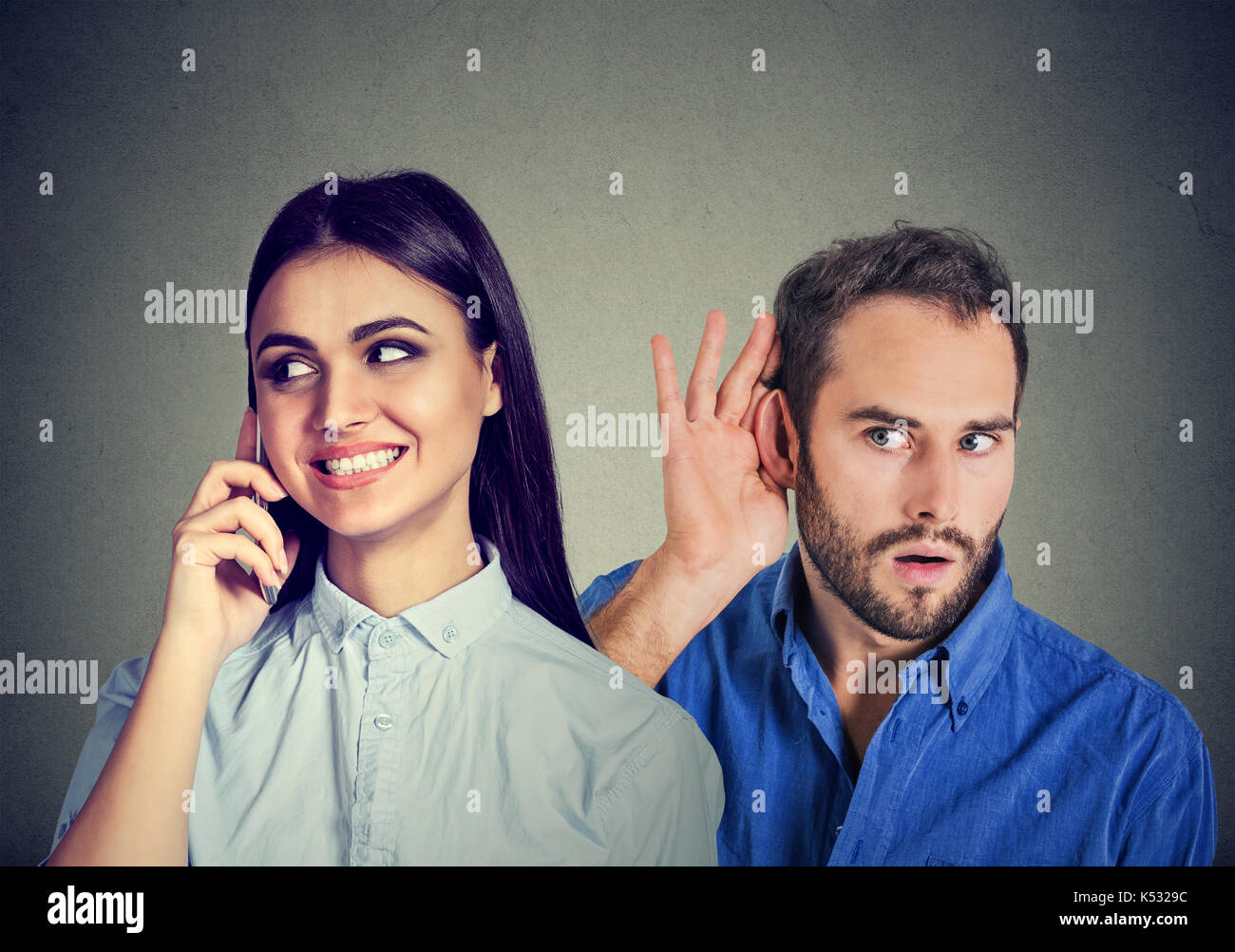Eine betrügende Freundin. Neugierig Mann heimlich zuhören eine glückliche Frau Gespräch am Handy mit Ihrem geliebten auf grauem Hintergrund Stockfoto