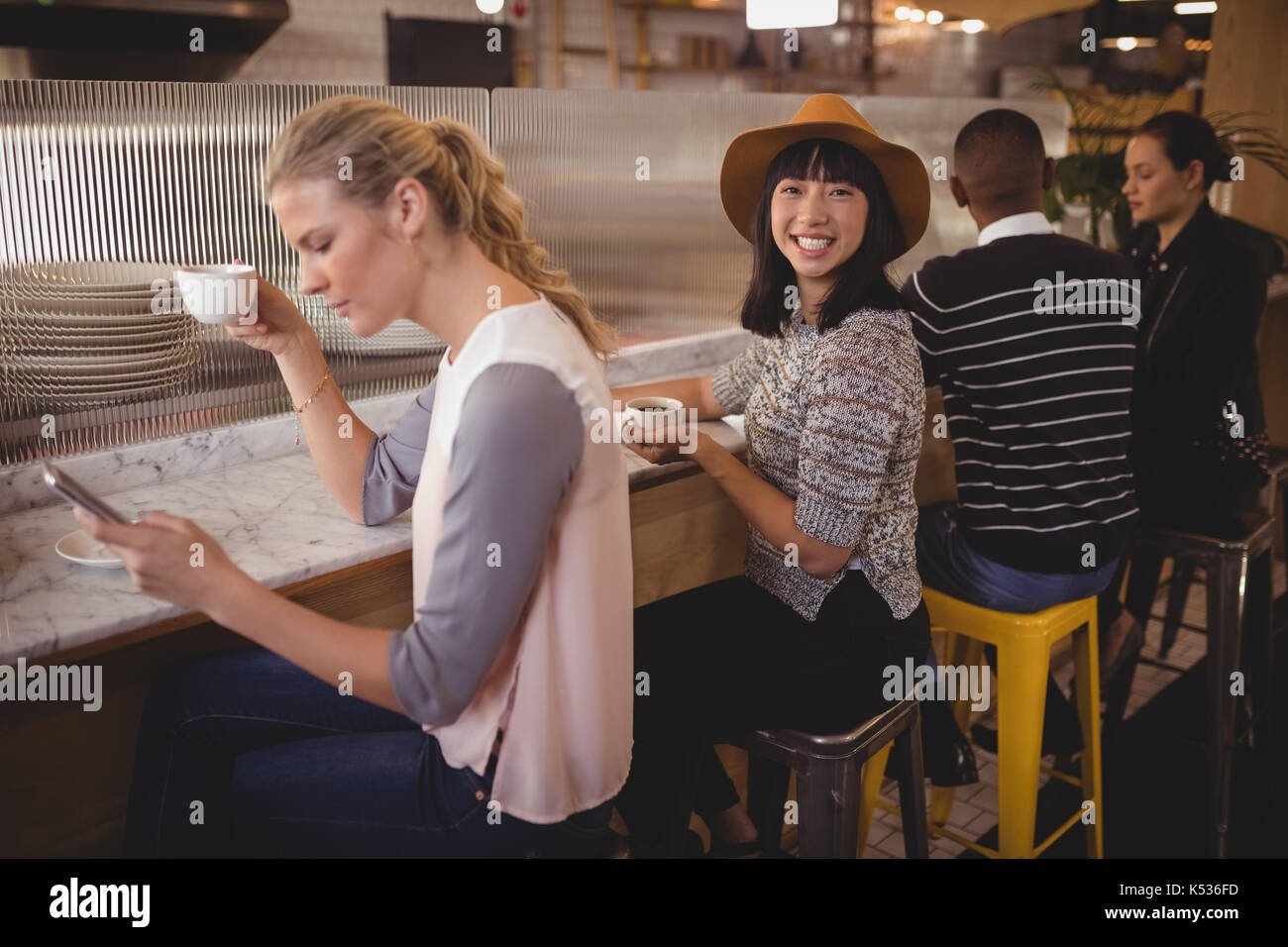 Portrait von lächelnden jungen Frau sitzt inmitten von Freunden an der Theke im Café Stockfoto