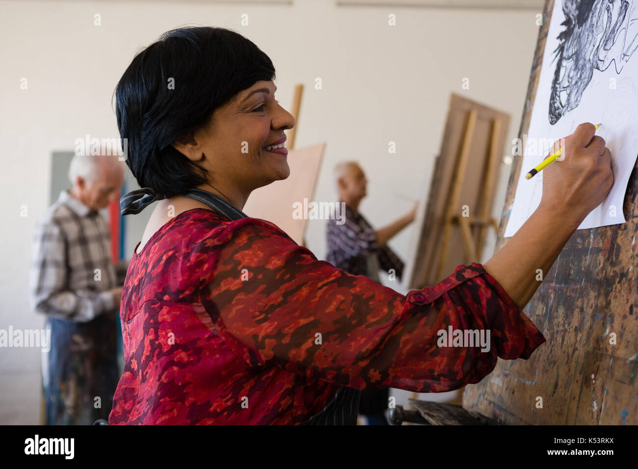 Der lächelnde Frau Malerei auf Papier mit Freund im Hintergrund bei Kunst Klasse Stockfoto