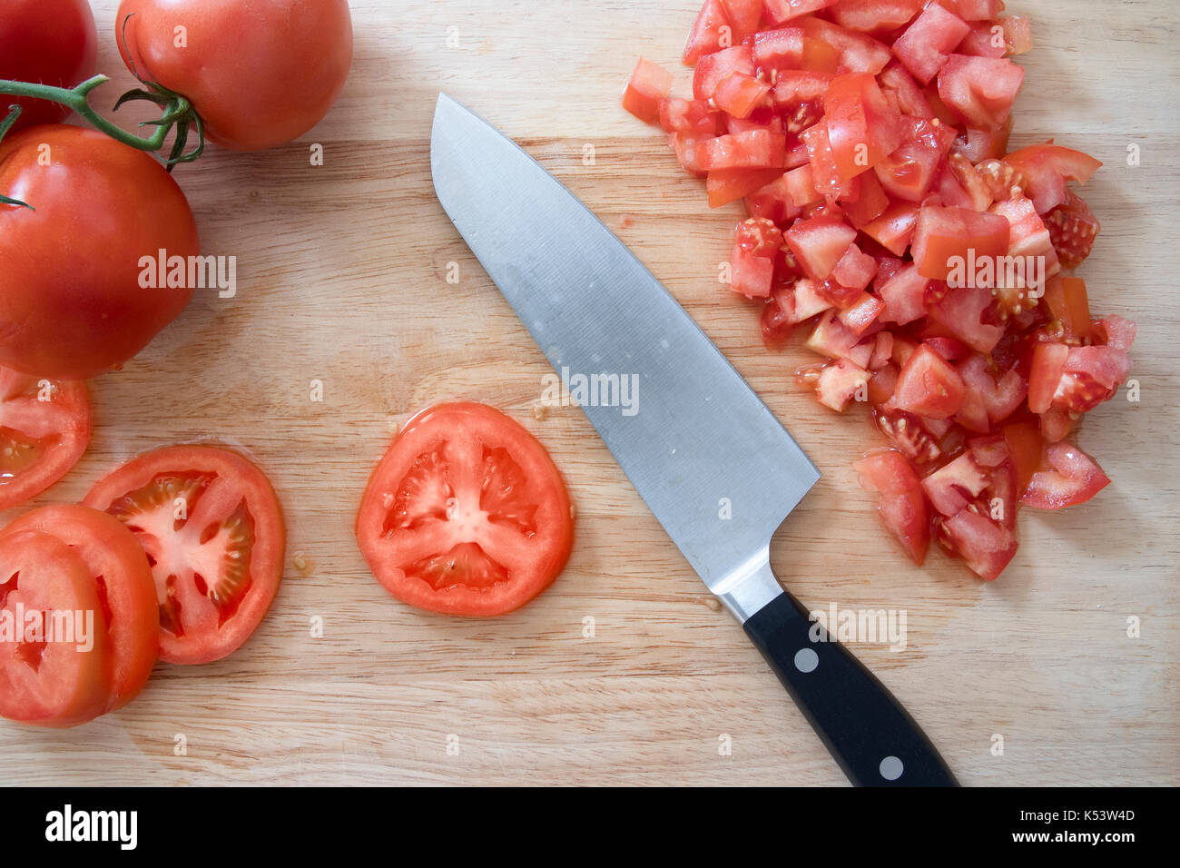 Tomaten/Paradeiser, ganz, in Scheiben geschnitten, gehackt, auf Schneidebrett mit Messer. Stockfoto