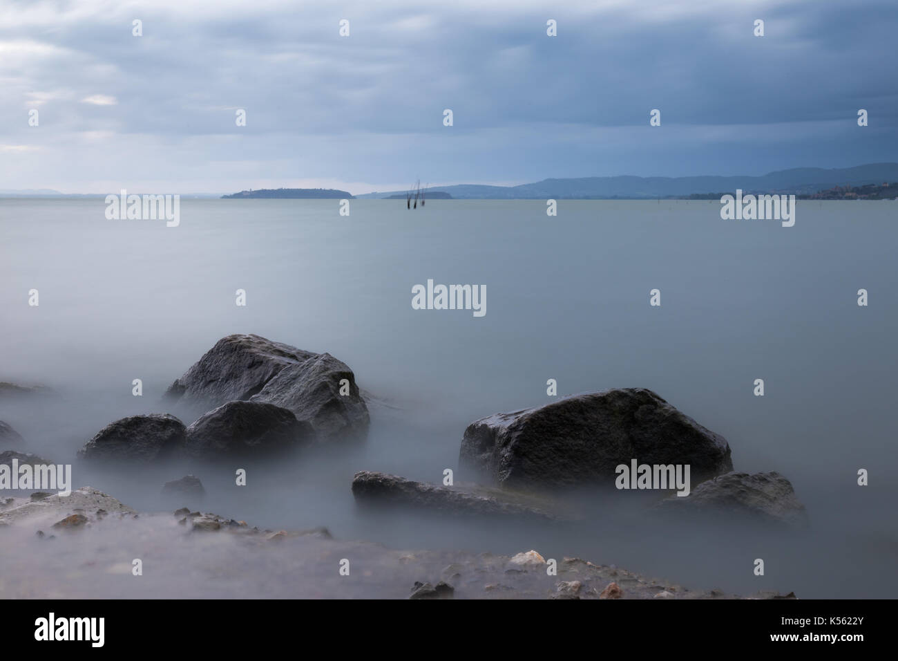 Eine minimalistische, Langzeitbelichtung Foto von einige große Felsen in einen See, mit perfekt noch Wasser und bewölkter Himmel Stockfoto