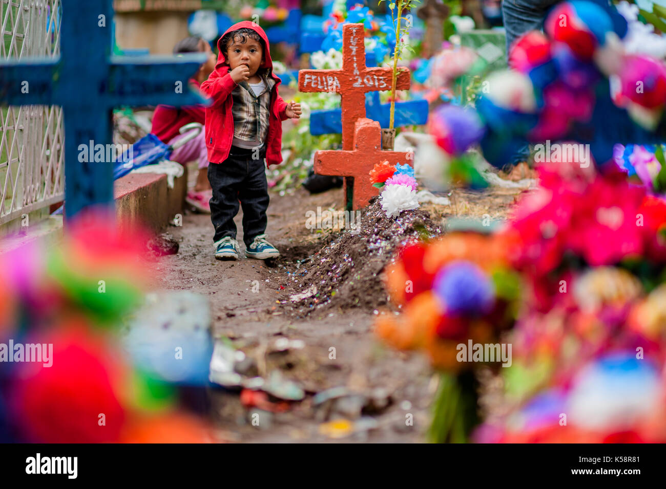 Eine Salvadorianische kid wartet auf seine Eltern unter Bunt geschmückte Gräber während der Tag der Toten Urlaub auf dem Friedhof in Izalco, El Salvador, 2. Stockfoto