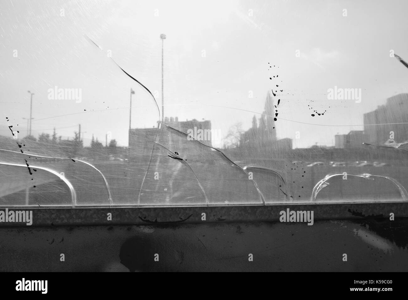 Entfernten Stadt Gebäude durch gebrochene Autobahn Barriere aus Glas. Abstrakte Buntglasfenster hintergrund Schwarz und Weiß verkratzt. Stockfoto