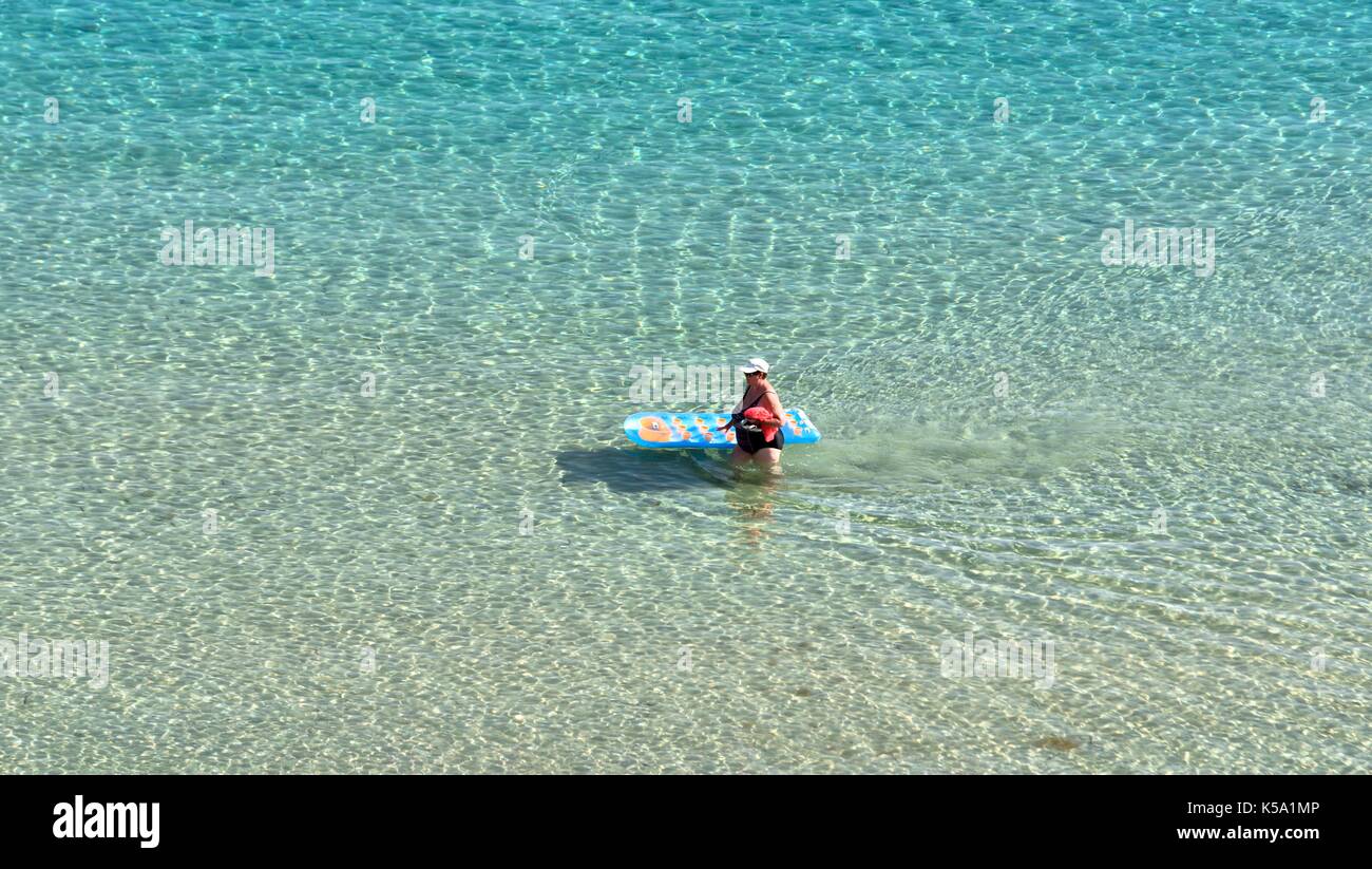 Eine Frau drückte eine blau und gelb Lilo durch seichtes Meer Wasser menorca Menorca Stockfoto