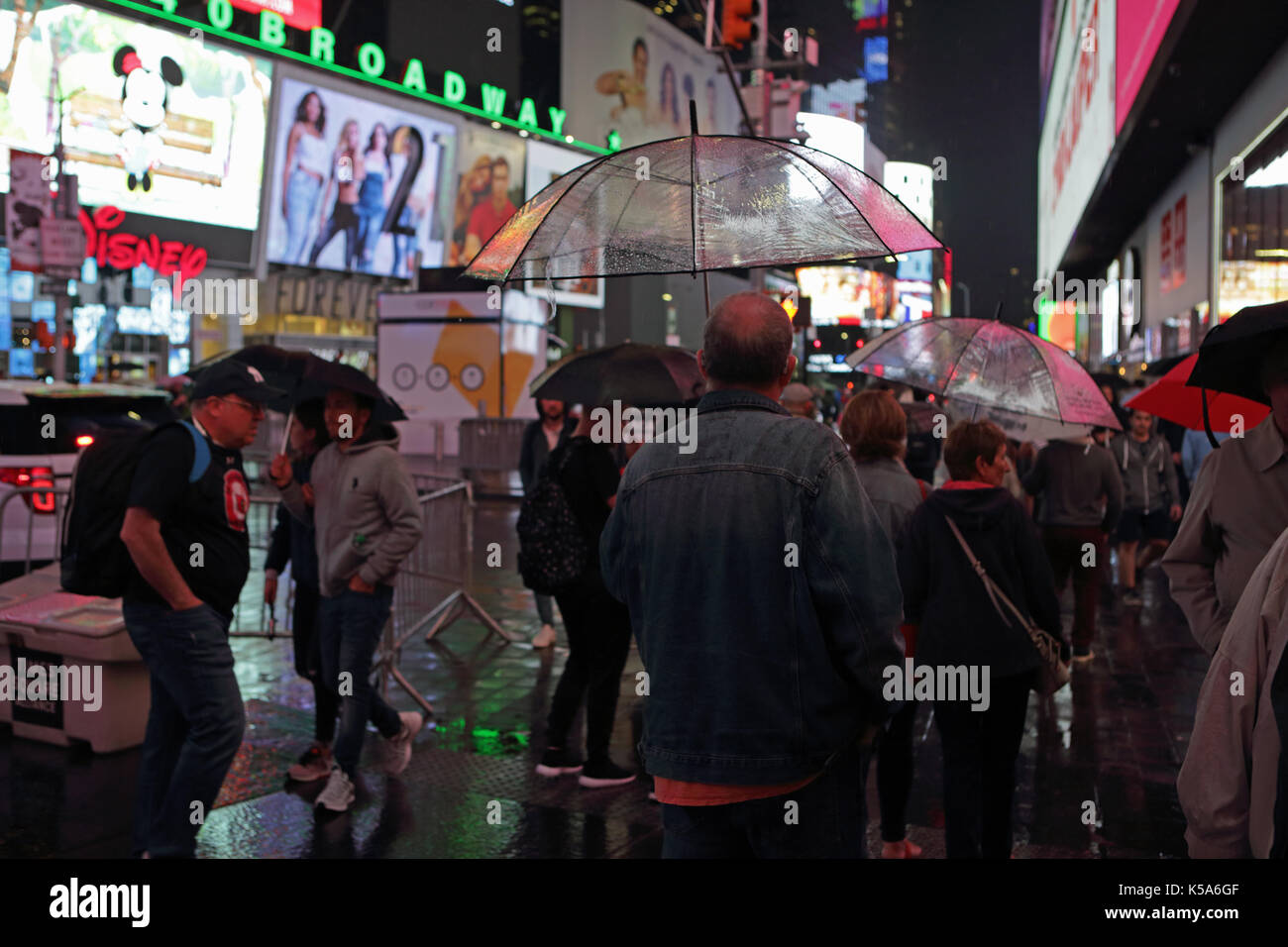 Regnerischen Nacht in Times Square, Touristen mit Sonnenschirmen gehen 7. Avenue und Broadway hell erleuchtet durch elektrische Plakatwerbung Bildschirme Stockfoto