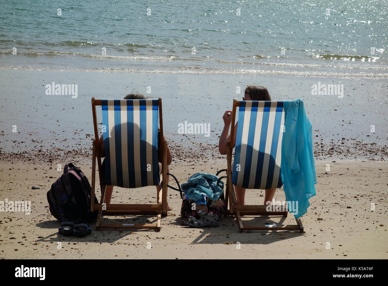 Die Frauen sitzen in Liegestühlen auf Clacton-on-Sea Strand Stockfoto