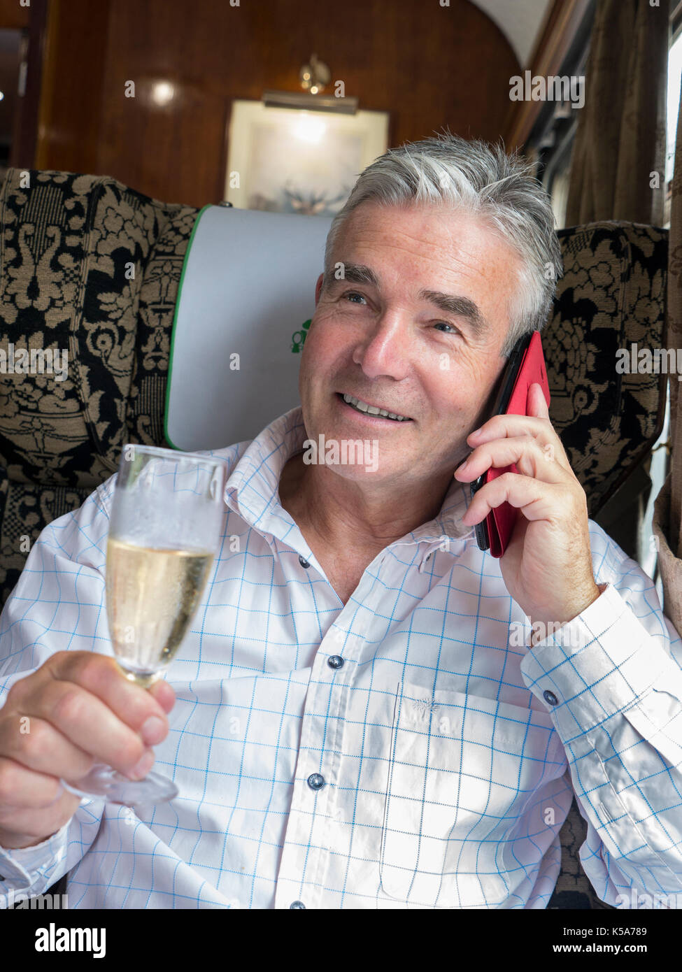 Luxus Champagner zug Mann mit einem Glas Champagner, über sein Smartphone, genießen eine Fahrt in der ersten Klasse vintage Pullman Waggon Stockfoto