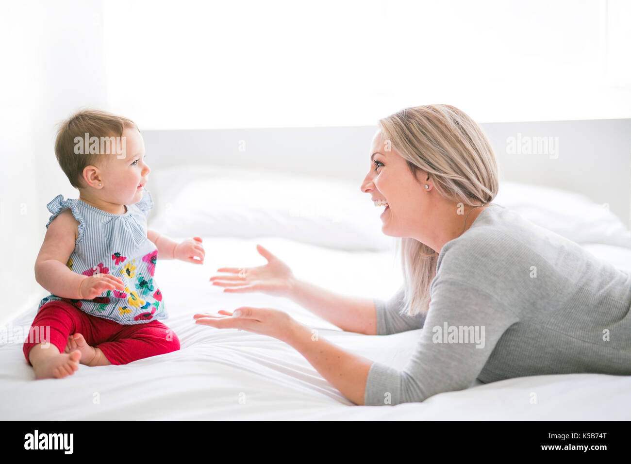 Hübsches Baby Sit-on-Mom im seidenen Bett Stockfoto