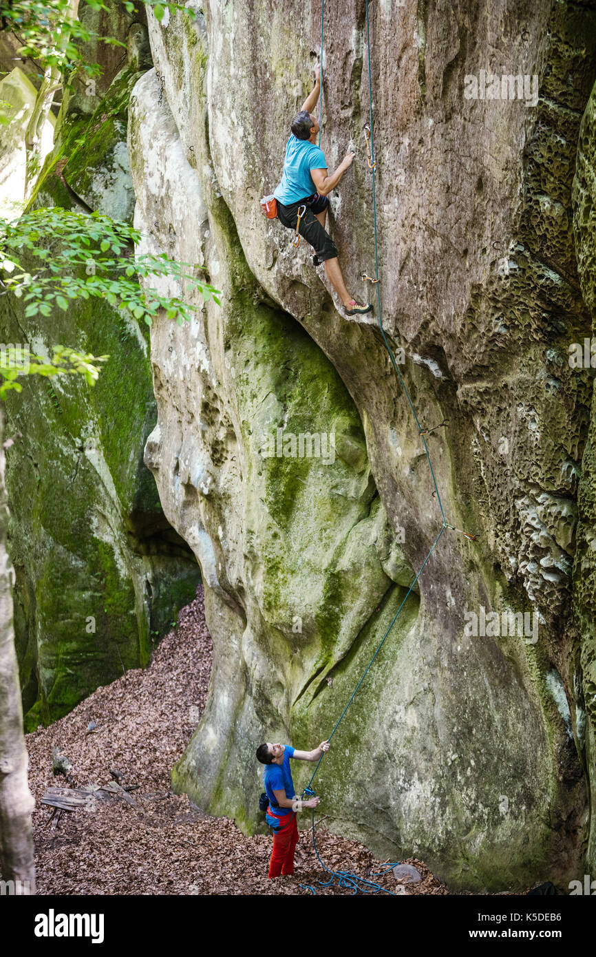 Junger Mann an der senkrechten Felsen, seinem Partner sichern. Top Rope klettern. Stockfoto