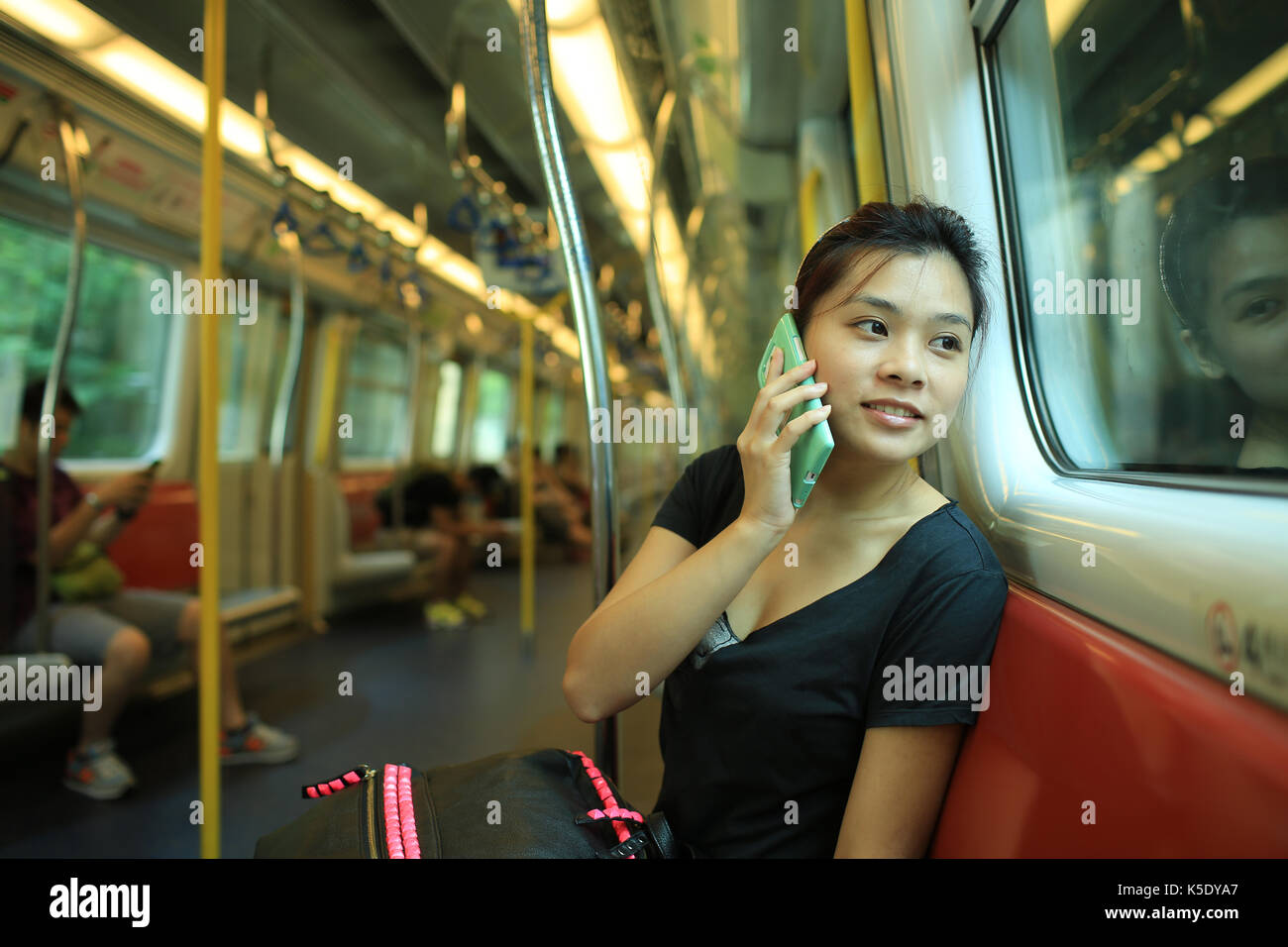 Nehmen Sie den Anruf klicken Sie auf das Reiseziel, sprechen auf smart phone mit guten Nachrichten, schöne Lady Watch außerhalb, Eisenbahn, Auto MTR, Hongkong, Chi Stockfoto