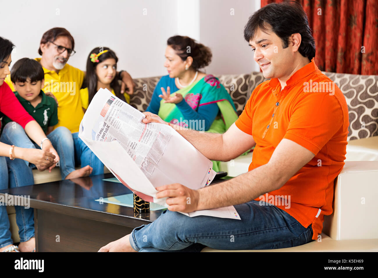 Glückliche Familie, Sitzen, Sofa mit ihren Mann lesen Zeitung in den Vordergrund zu Hause Stockfoto