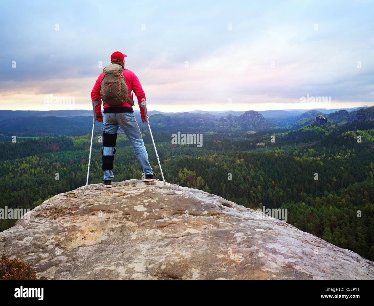 Behinderte Menschen mit Krücken steht auf einem großen Felsen und Blick in die Berge am Horizont. Wanderer Silhouette mit Medizin Krücke auf Berggipfel. Stockfoto