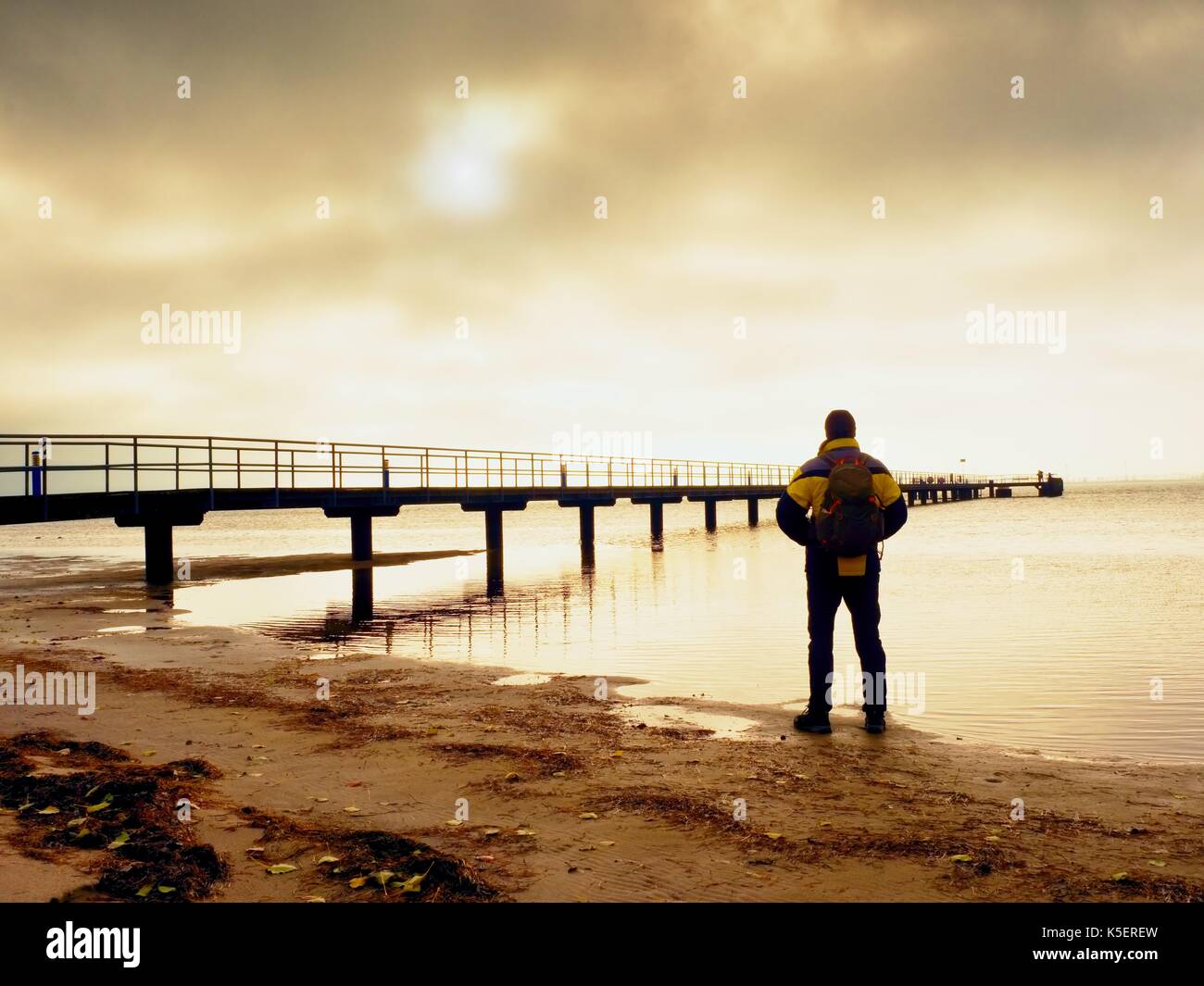 Rückansicht des Tourist in trekking Kleidung am Strand am Pier. Gradient Sunset View Hintergrund Stockfoto