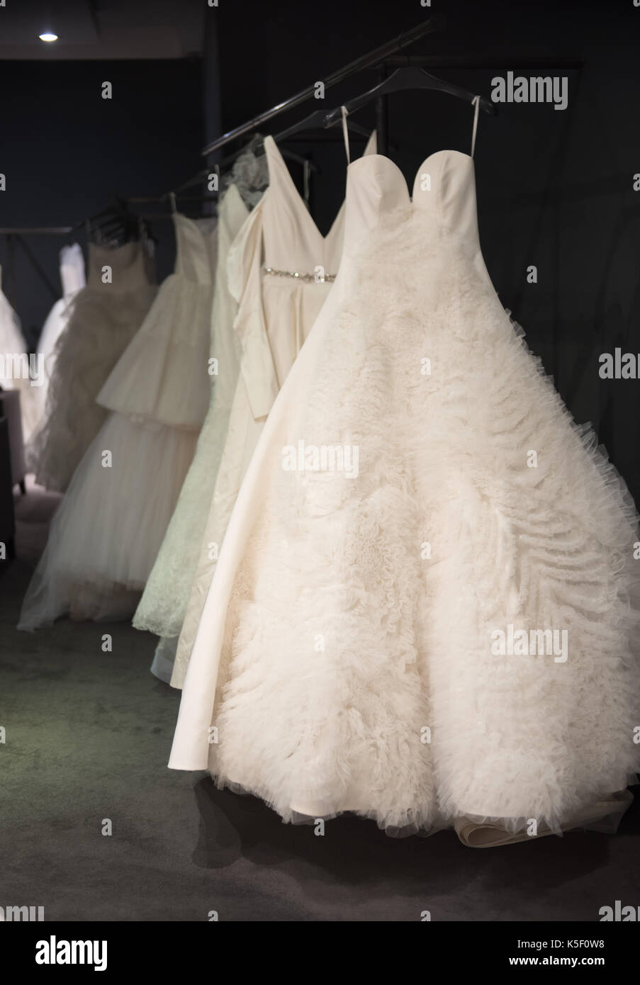 Auswahl der weiße Brautkleider und Ballkleider auf Anzeige hängen auf Schienen mit selektiven Fokus auf einer beleuchteten durch ein Highlight Stockfoto