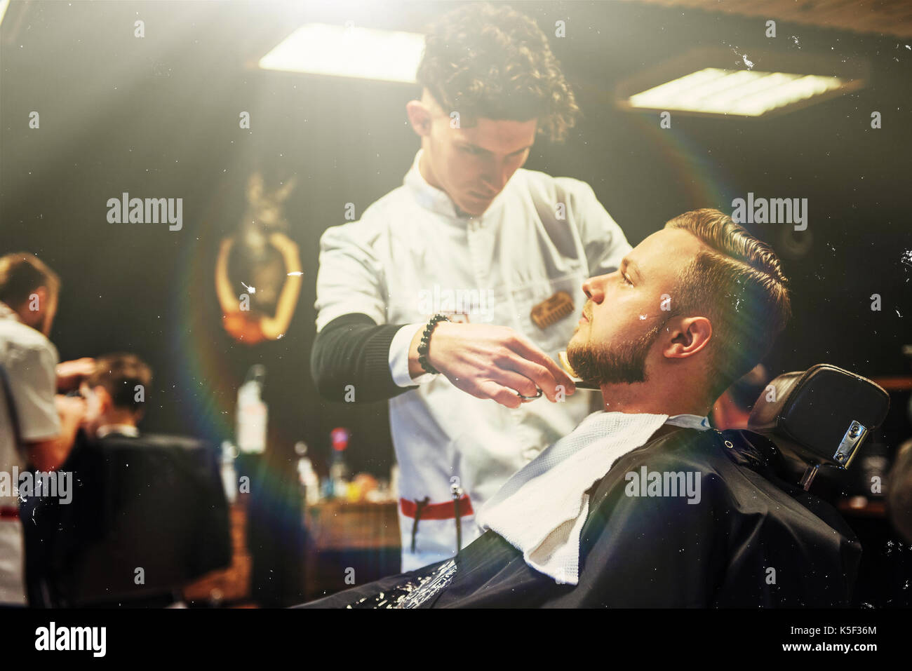 Der Friseur Mann in den Prozess der Schneiden der Bart des Client elektrische Haarschneidemaschinen im barbershop. Stockfoto