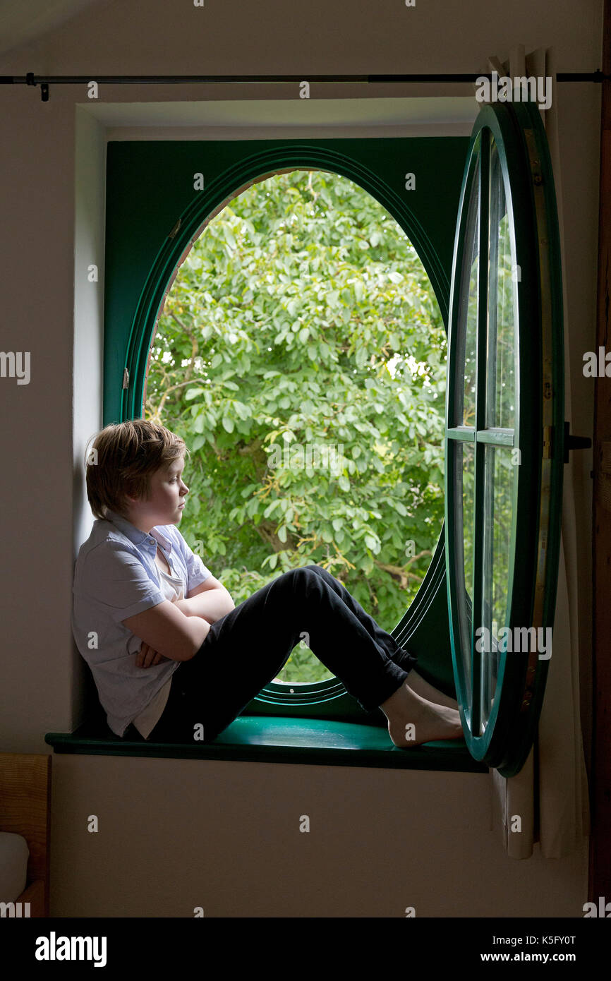 Kleiner Junge sitzt in einem Fenster Stockfoto