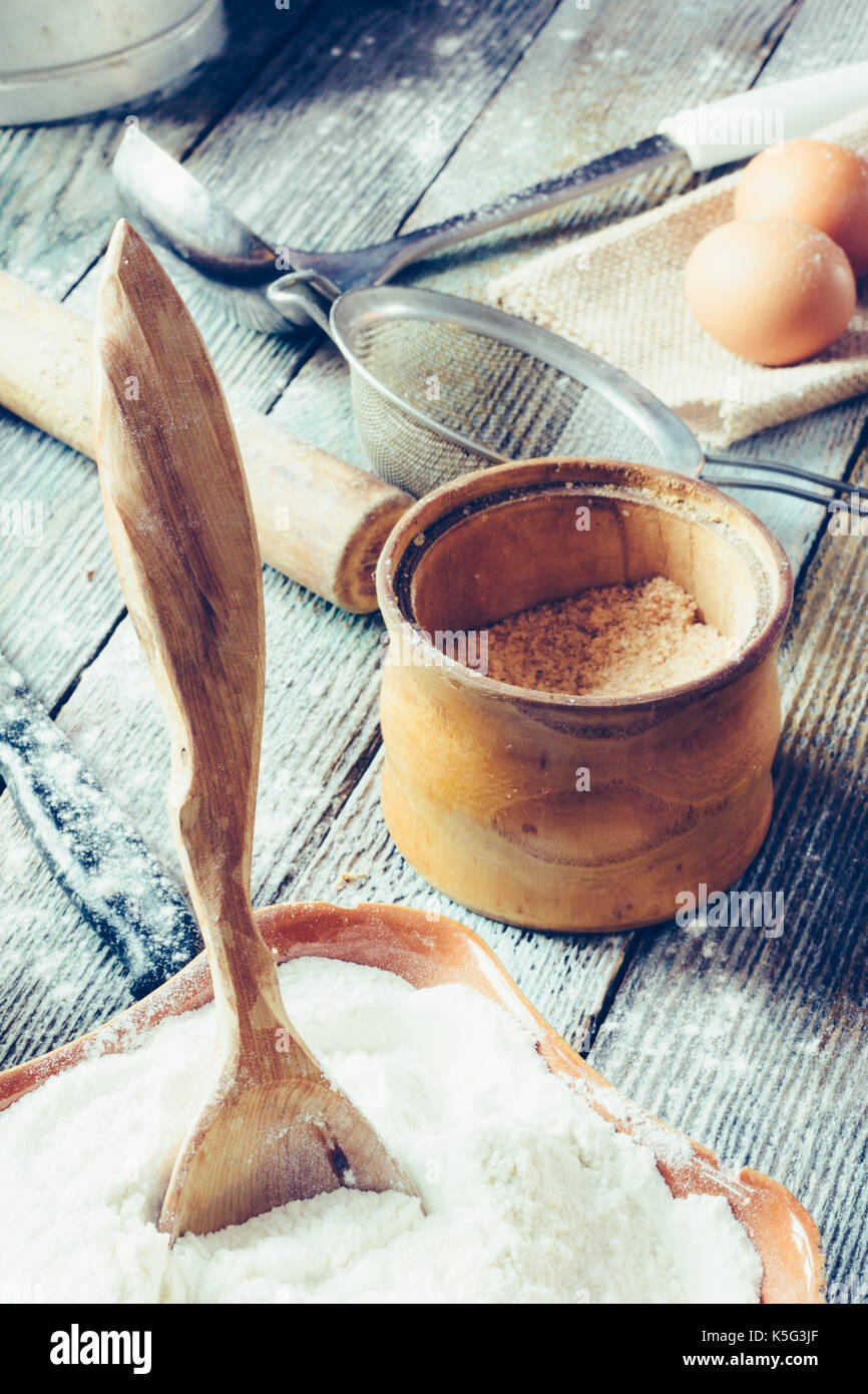 Die hölzernen Löffel an die keramische Schüssel mit dem Mehl, Bank mit Adyghe Salz, Eier, Nudelholz, Metall Sieb und eine Kelle. Konzept rustikale Küche, Küche Stockfoto